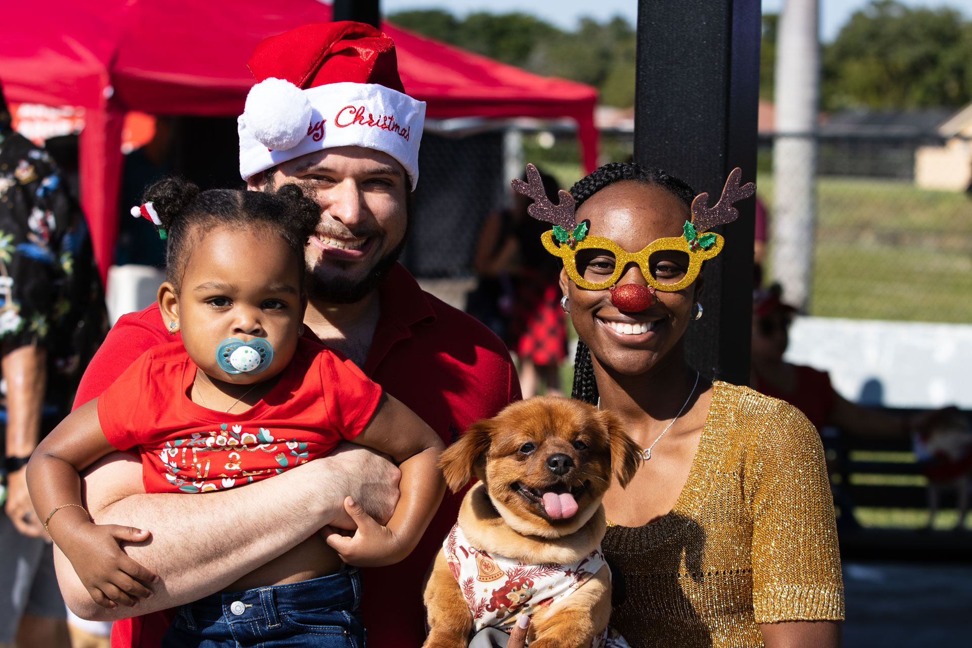 Three people wearing red and green festive colors and a brown dog with its tongue hanging out 